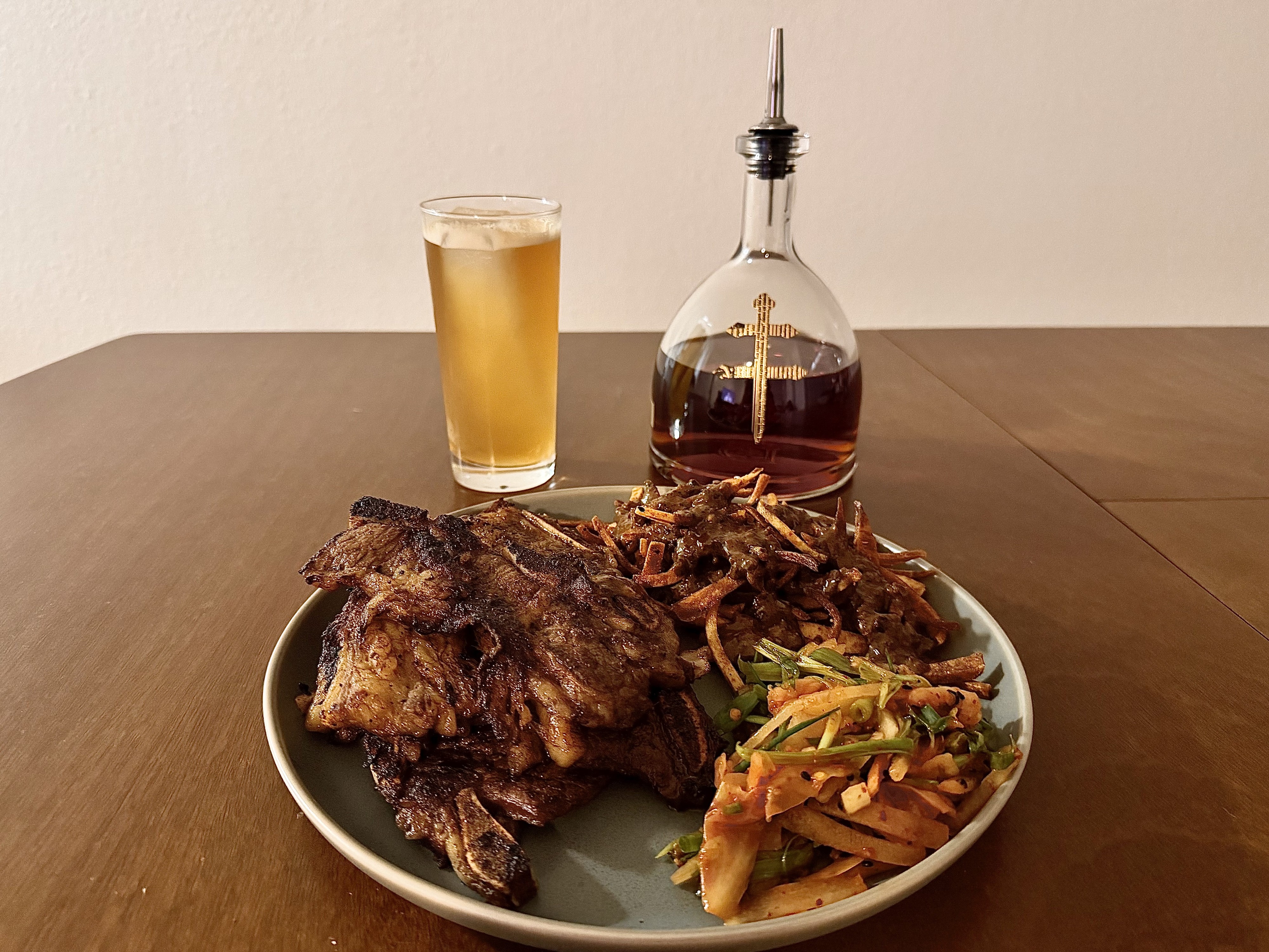 Galbi short ribs, triple-cooked fries, and Asian pear salad on a plate, with a beer and decanter behind it