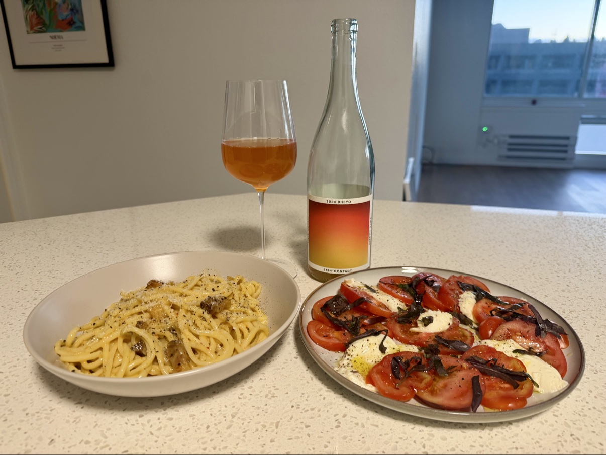 Bowl of carbonara next to a caprese salad plate, with a glass and bottle of skin-contact white wine