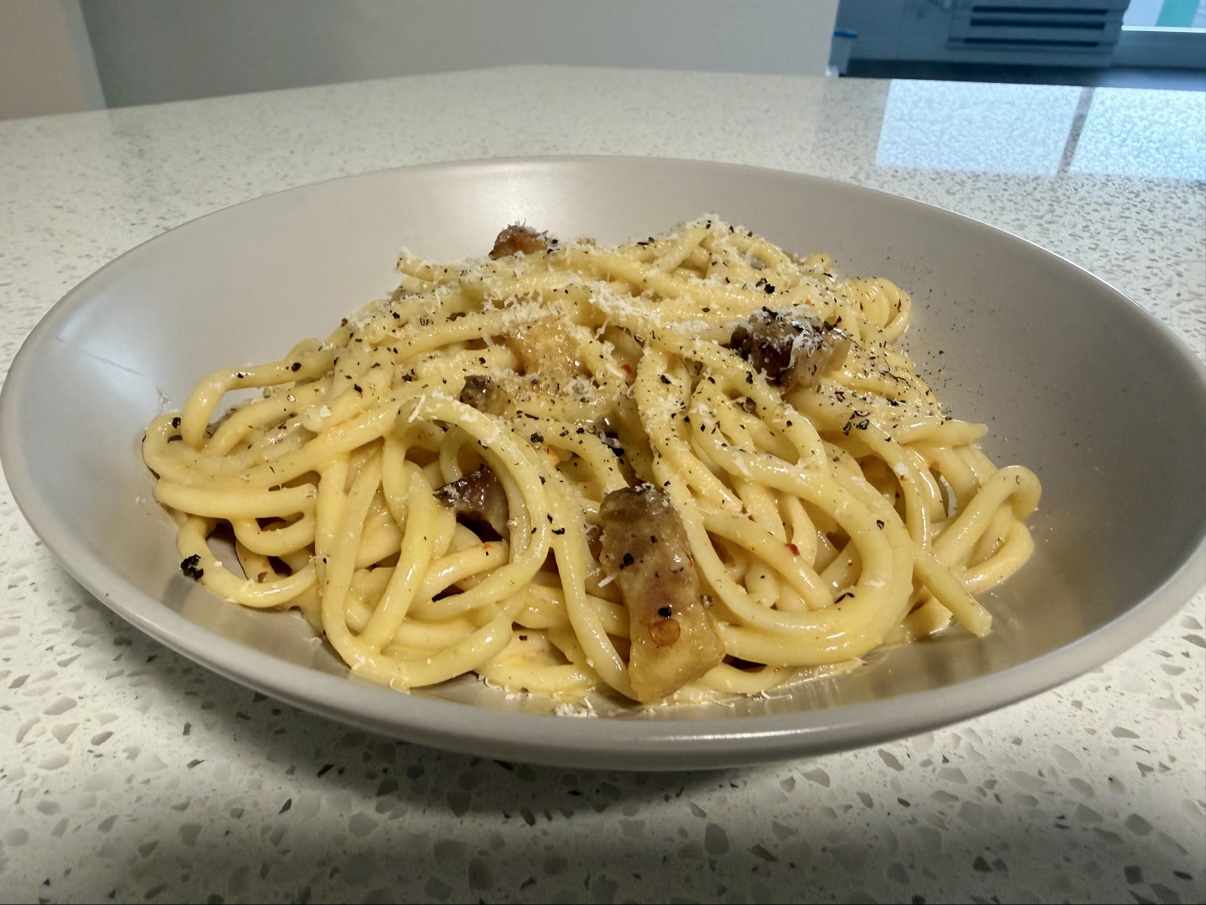 Close-up of bucatini carbonara with guanciale, grated cheese, and cracked black pepper